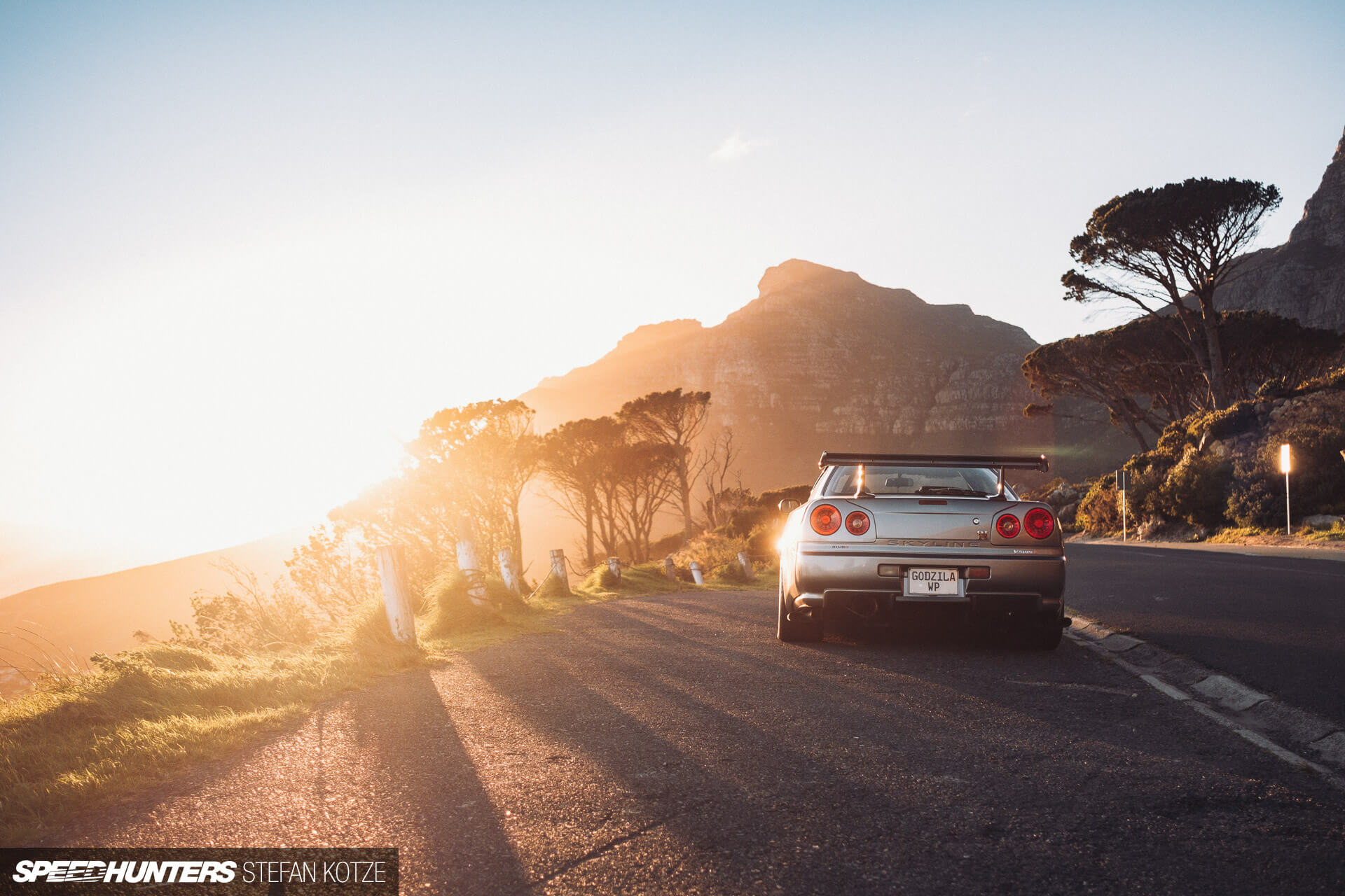 Nissan Skyline R34 GT-R on the side of a 
                    mountain road with a sunset backgound